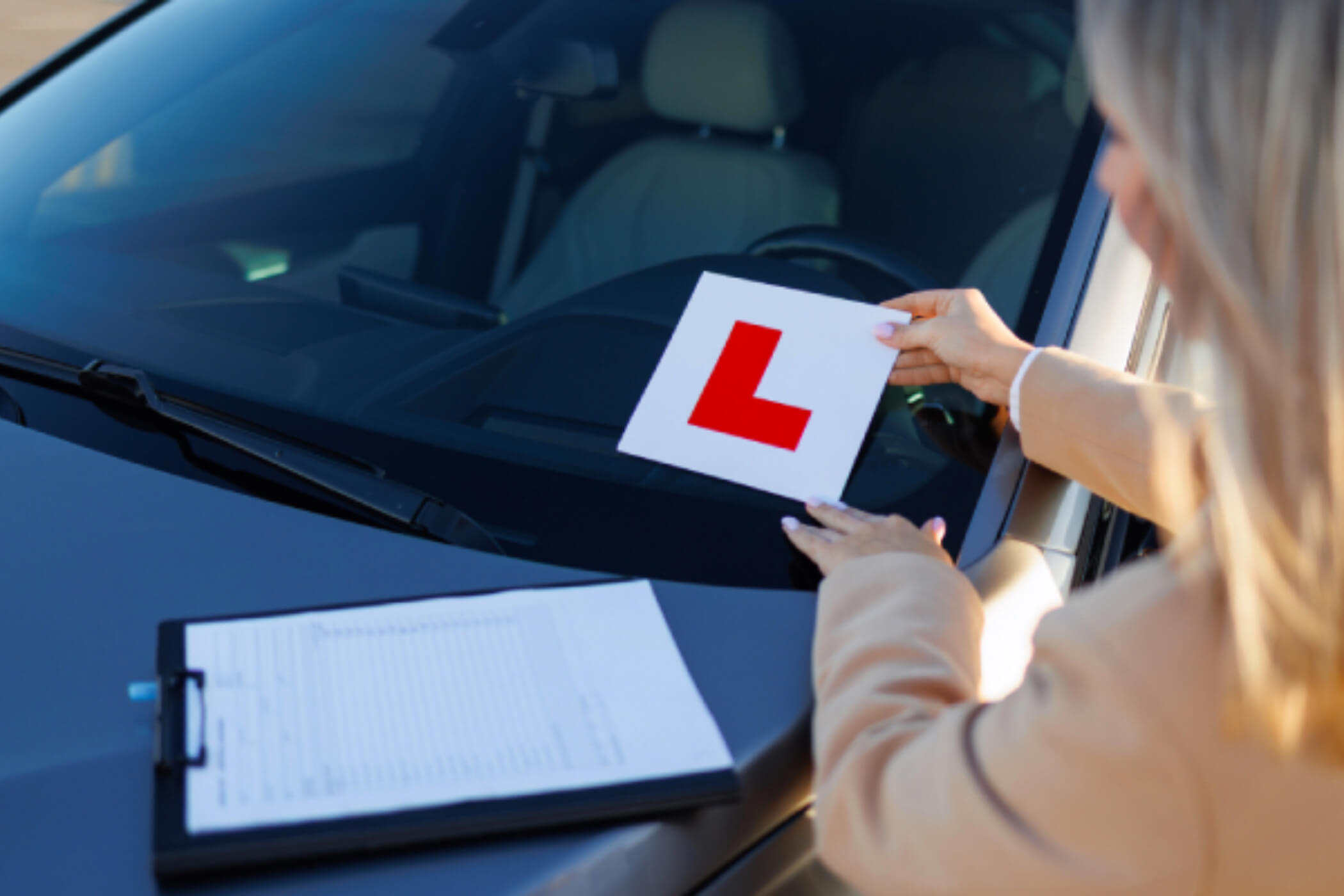 Woman placing L-plate onto windscreen of a car