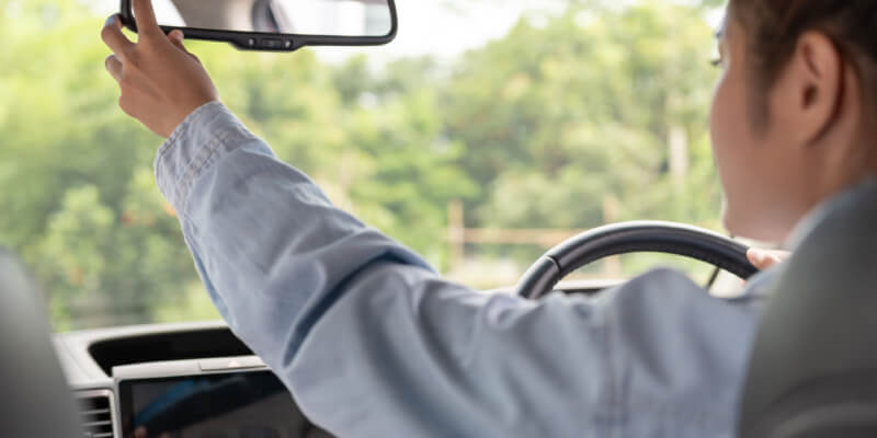 Girl reaching to adjust rearview mirror in car